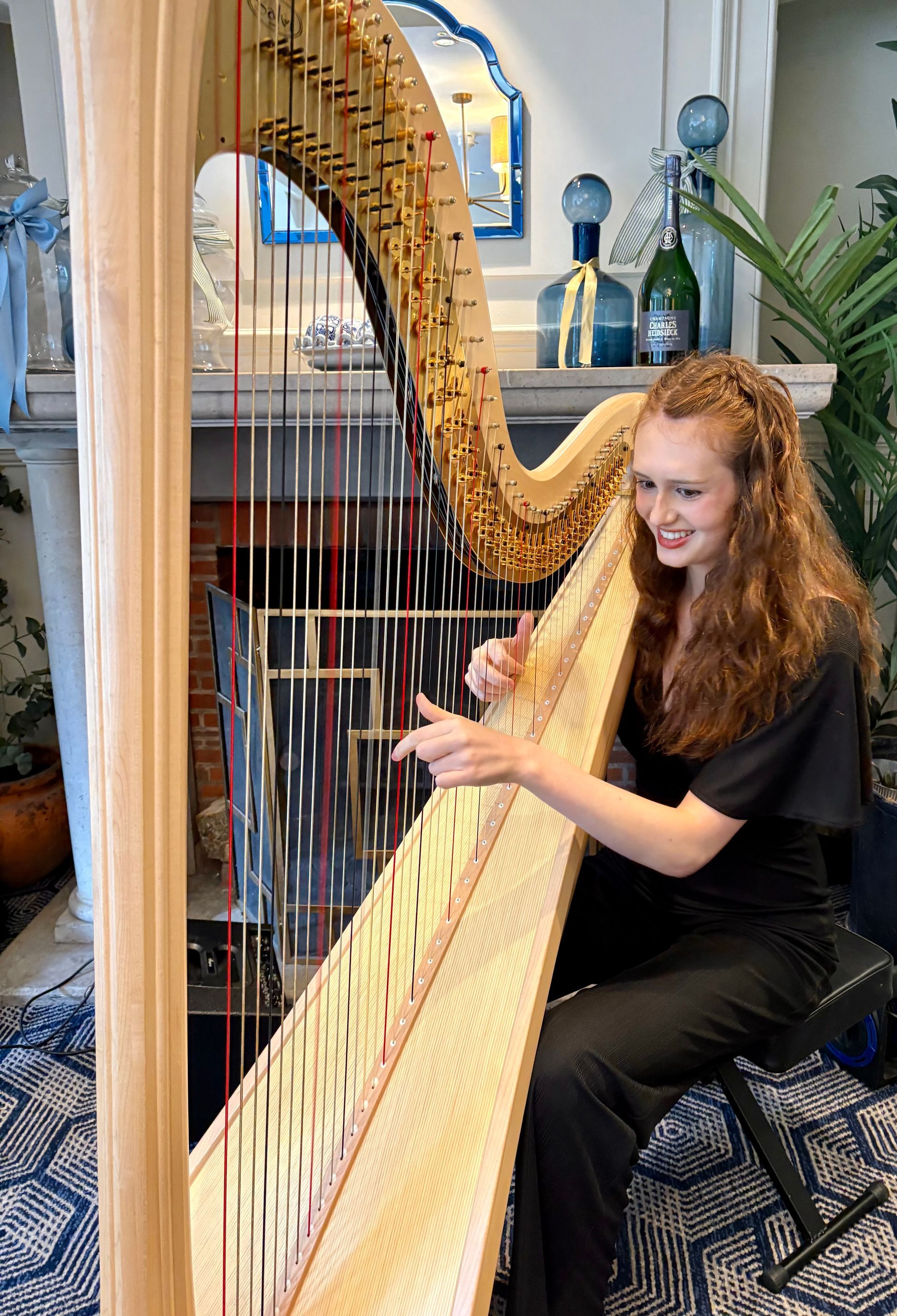 Woman playing a tall golden harp in a bright room with bookshelves and patterned carpet