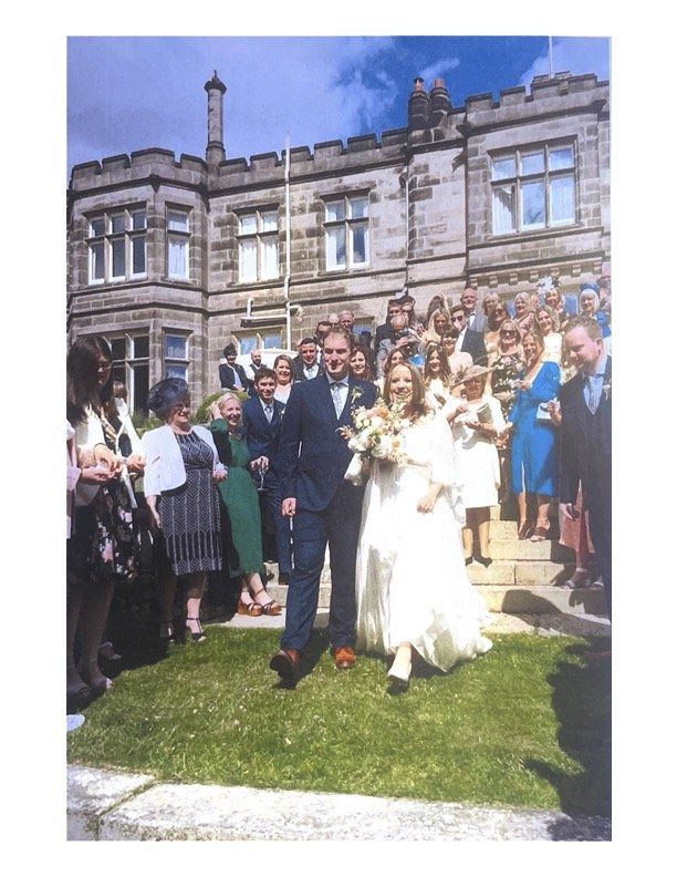 Bride and groom walk through a cheering crowd outside a stone building at a wedding