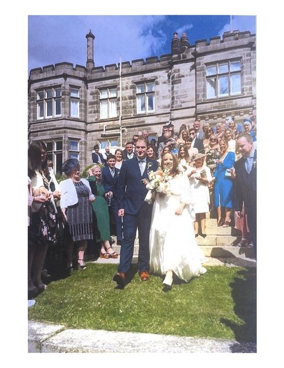 Newlyweds exiting a stone building after a ceremony, smiling, surrounded by guests.