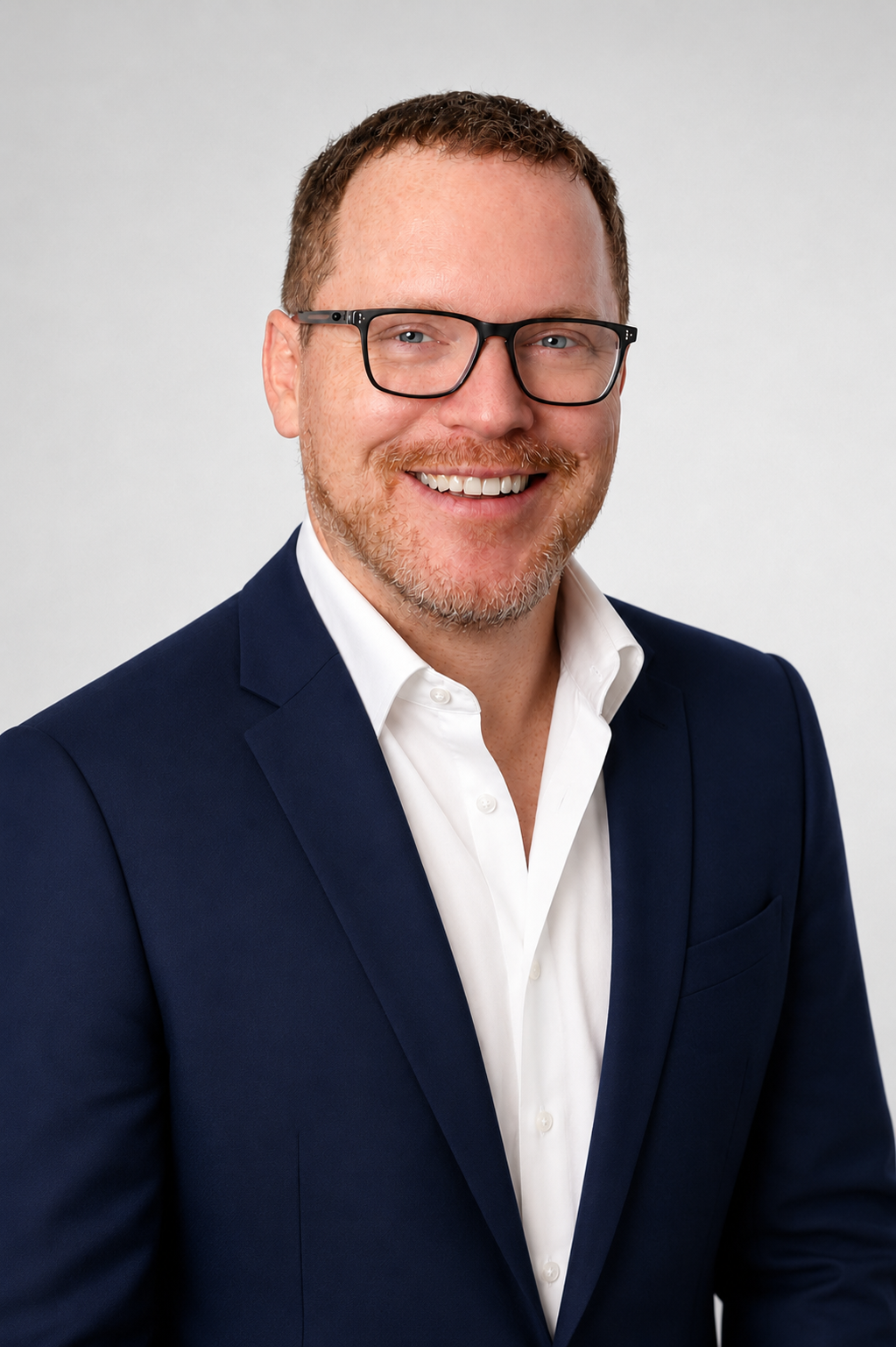 A man in a blue suit and glasses is smiling for the camera.