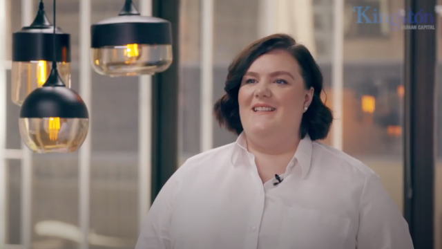 A woman in a white shirt is smiling in front of a window.