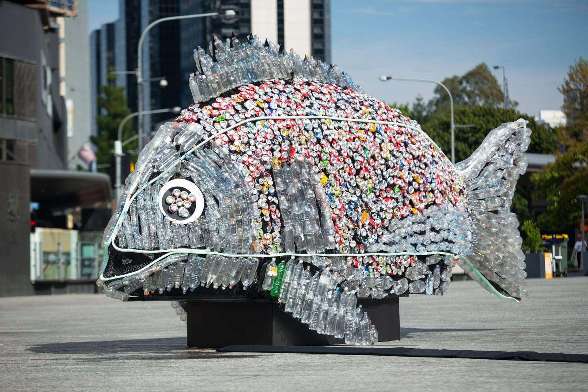 A statue of a fish made out of plastic bottles in a city.