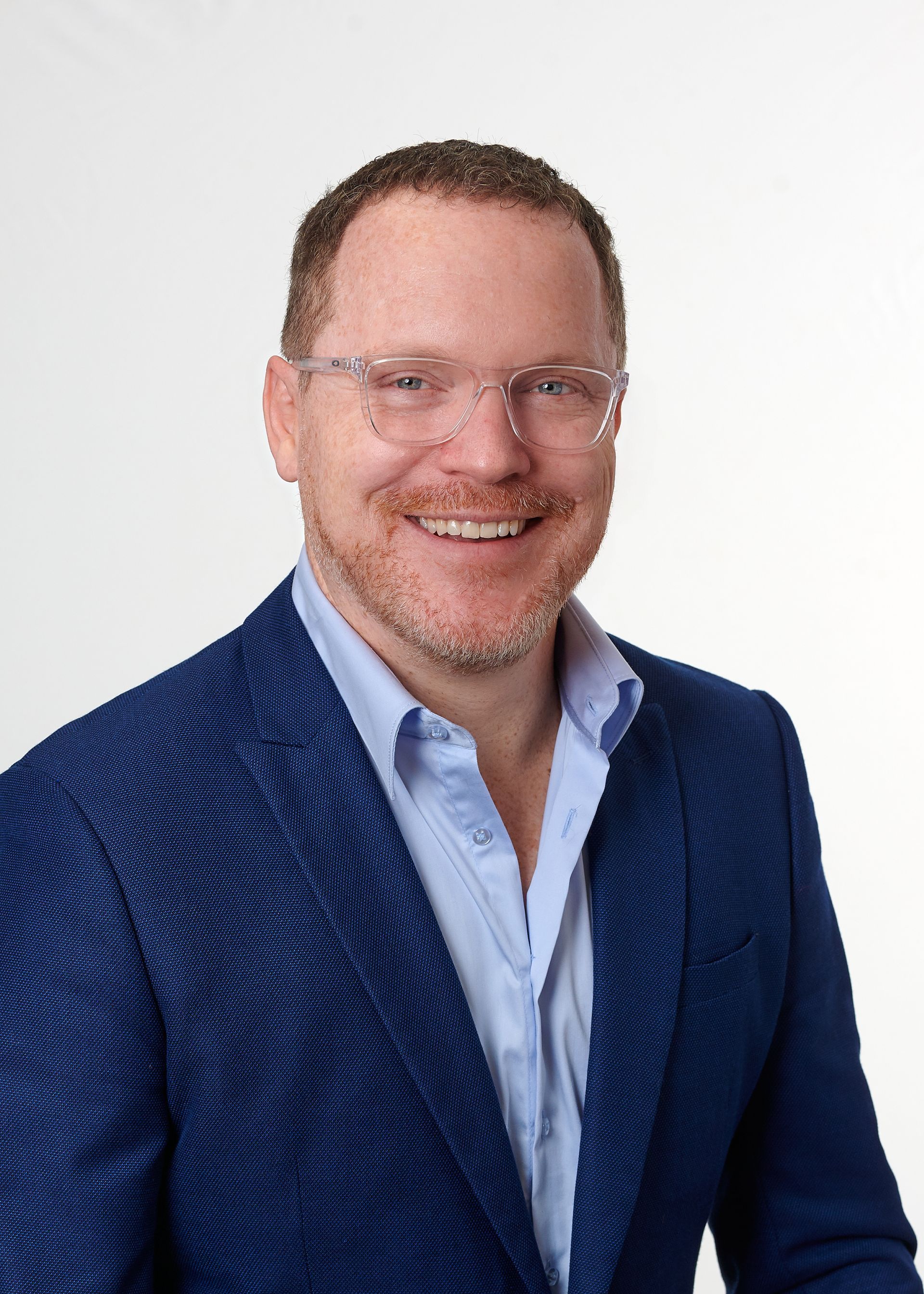 A man in a blue suit and glasses is smiling for the camera.