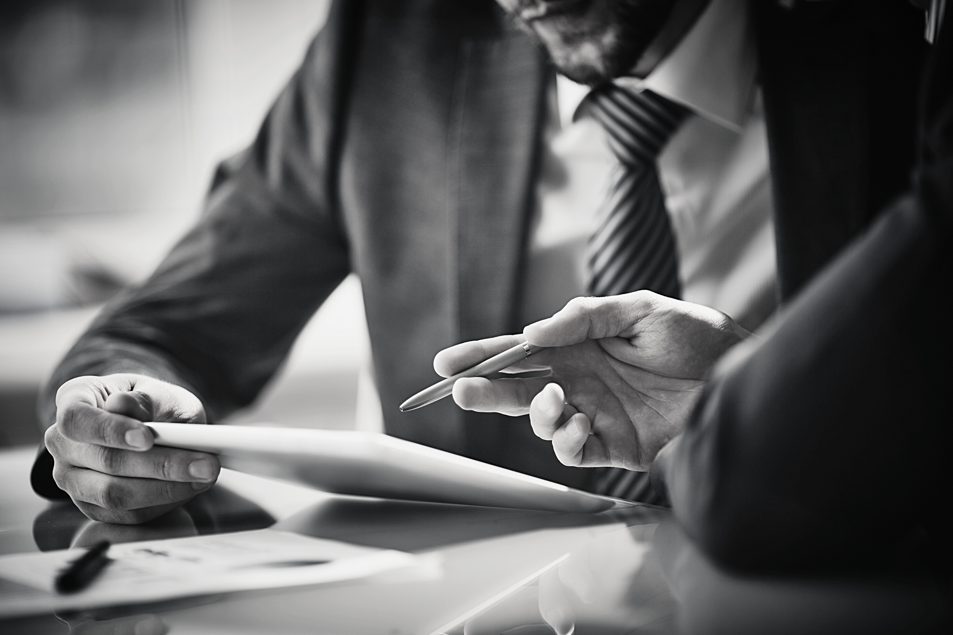 A man in a suit and tie is holding a pen and looking at a tablet.