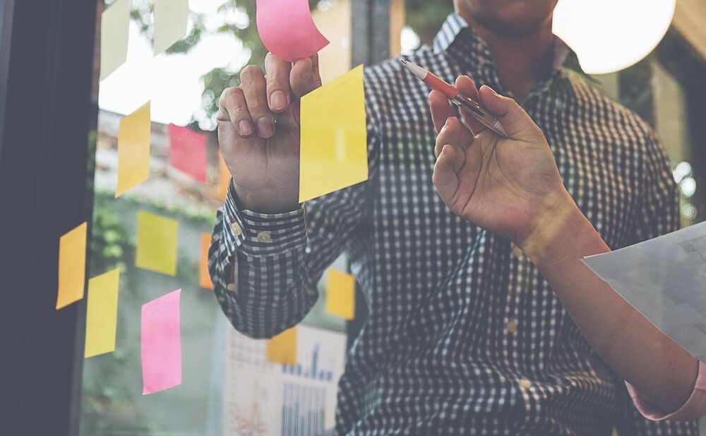 A man is writing on a glass wall with sticky notes.