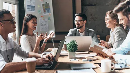A group of people are sitting around a table with laptops.
