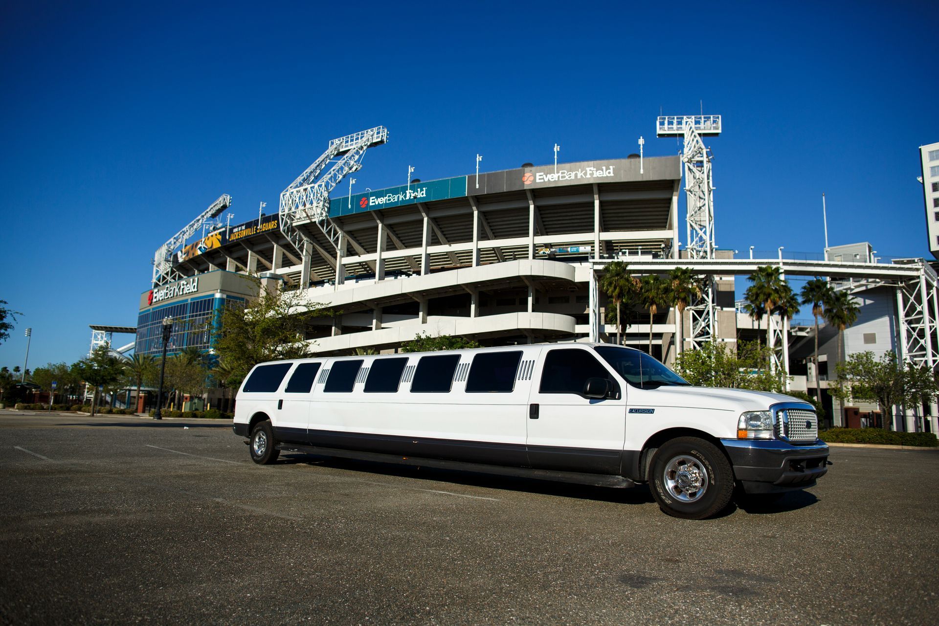 White stretch limousine parked outside a stadium under a clear blue sky