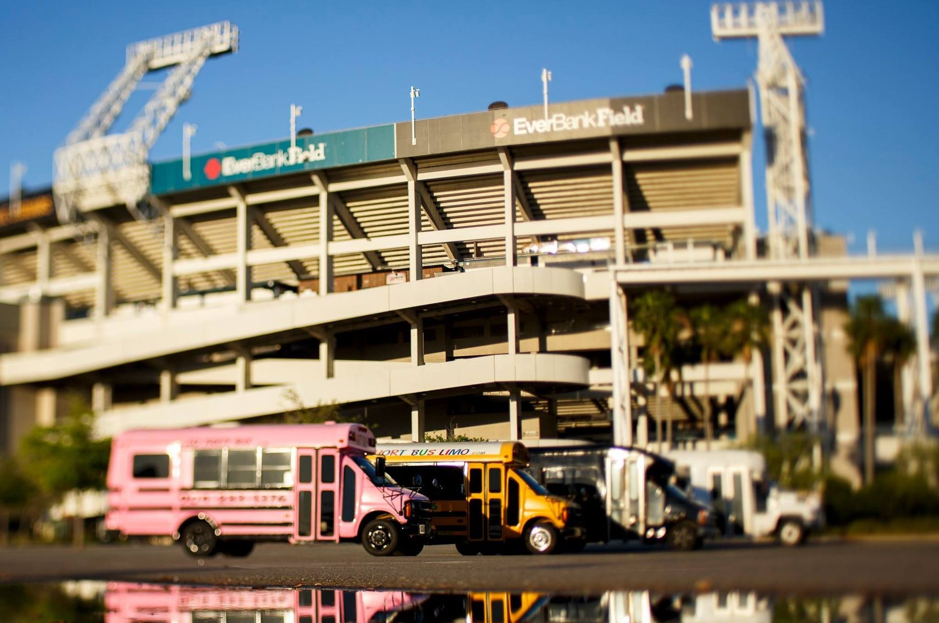 Buses and a pink van parked outside a stadium with visible signs and steel framework