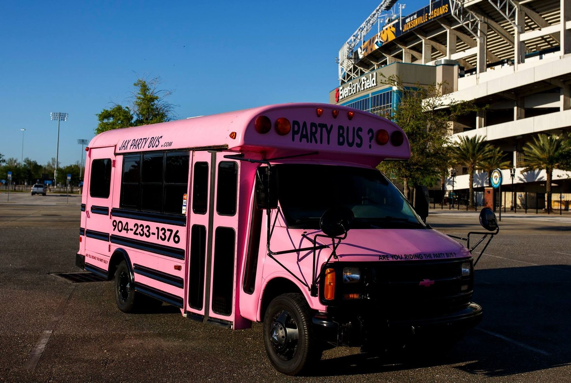 Pink party bus parked outdoors near a stadium, with “PARTY BUS” on the side.