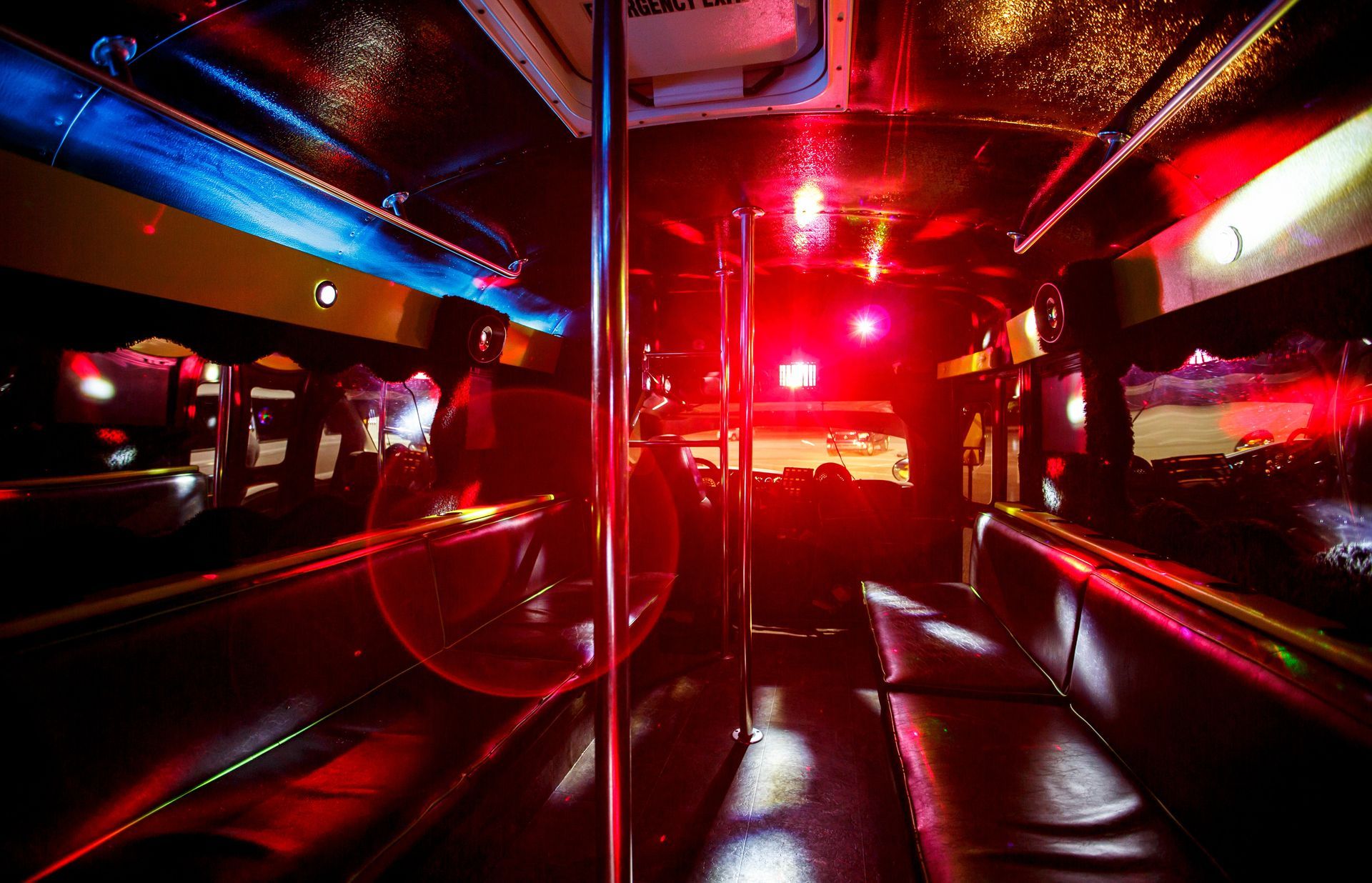 Inside a neon-lit bus at night, with red and blue lights reflecting on seats and windows