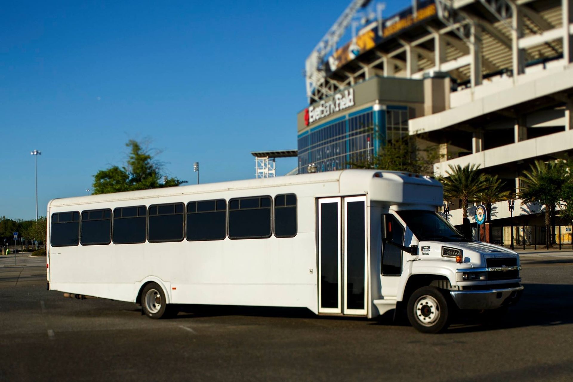 White shuttle bus parked outside a stadium under a clear blue sky