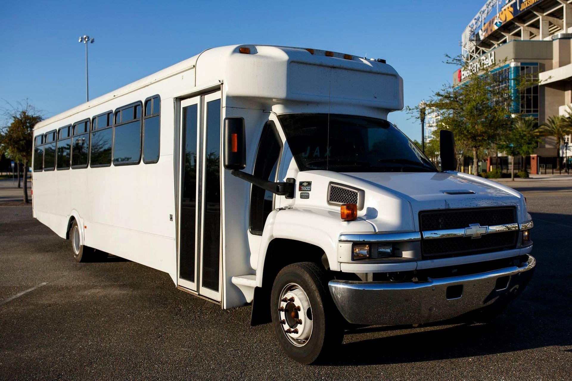 White shuttle bus with an extended passenger body parked outdoors on a sunny street.