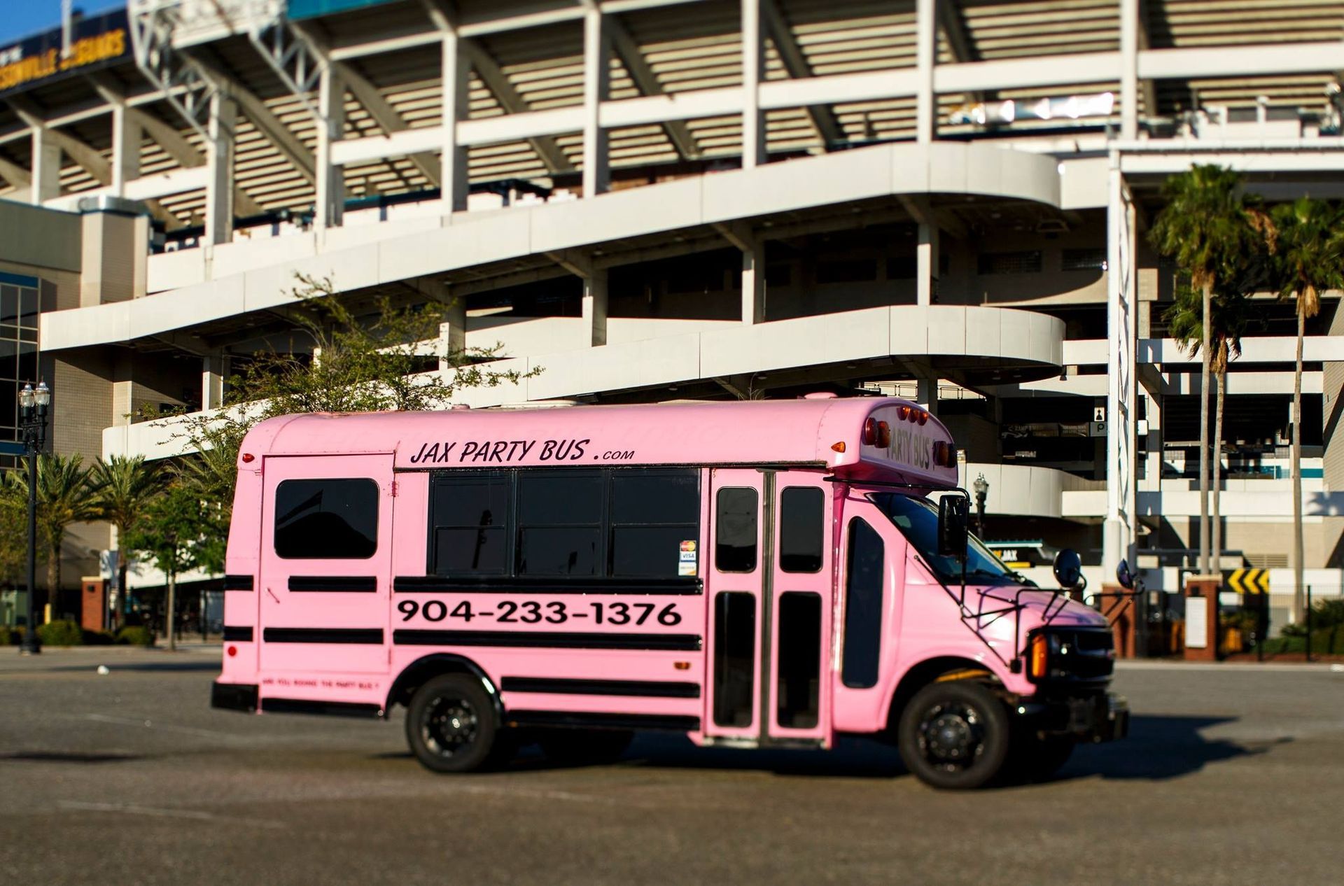 Pink shuttle bus parked in front of a multi-level building, with a phone number on the side
