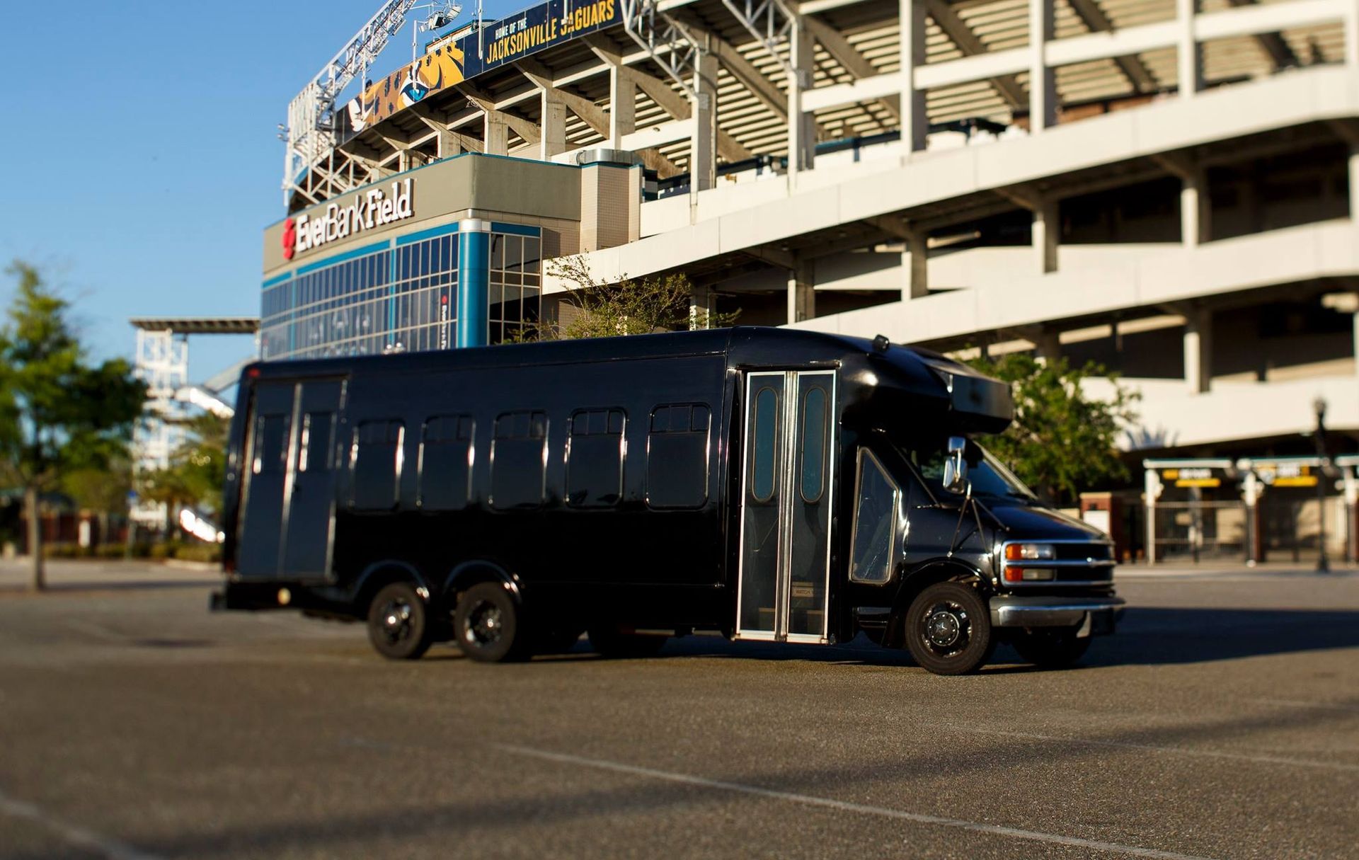 Black coach bus parked beside a stadium on a sunny day