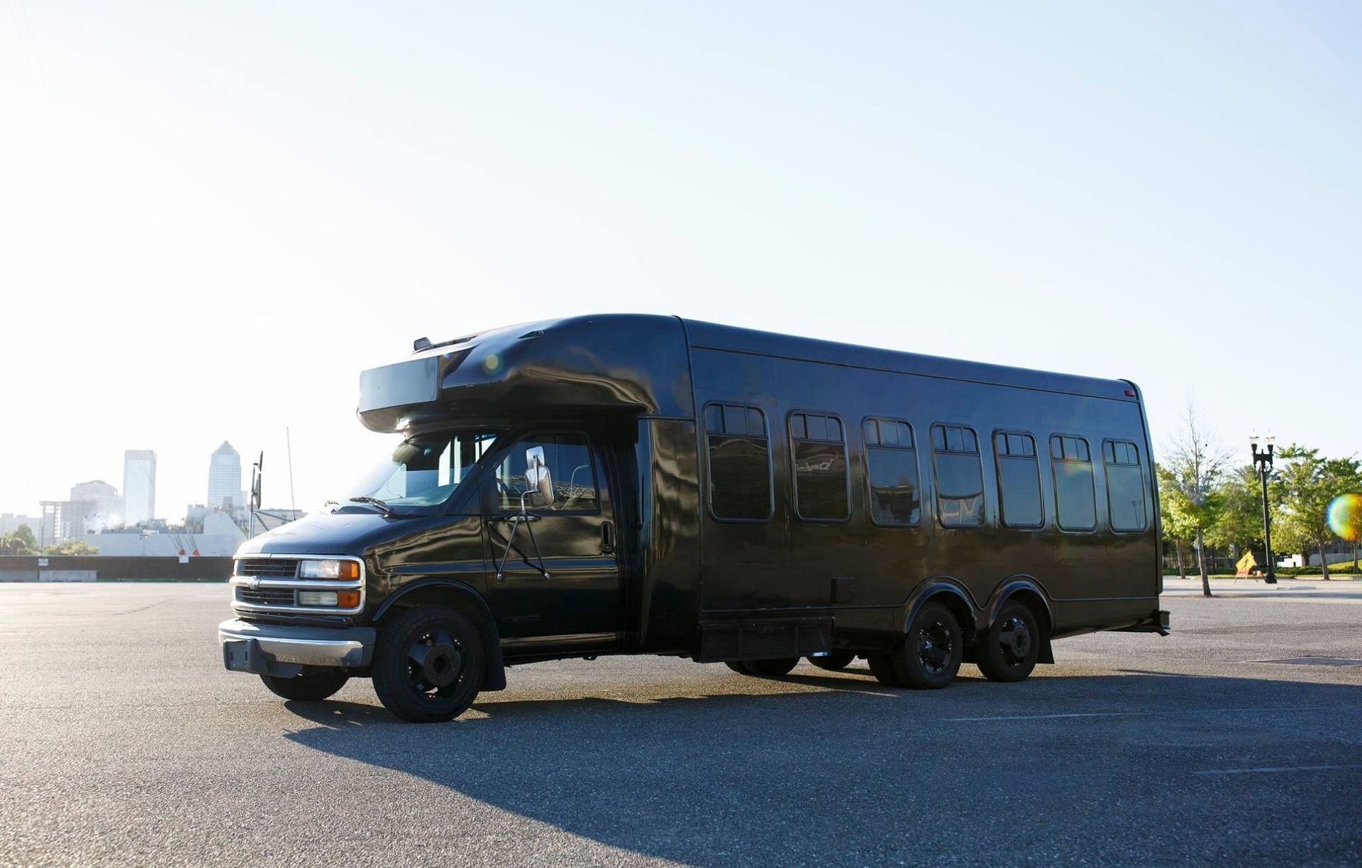 Black bus parked on a paved lot with city buildings in the distance