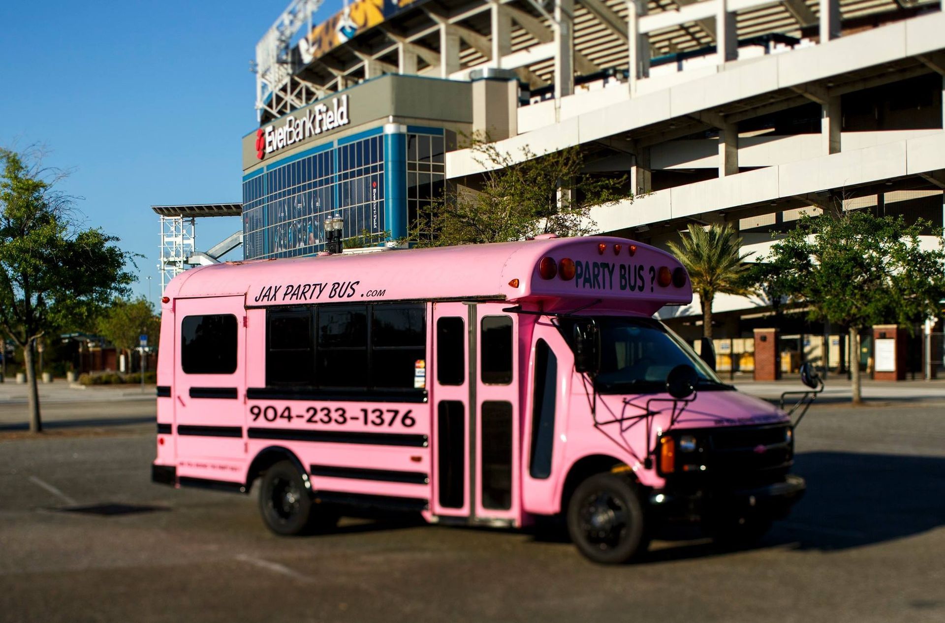 Pink shuttle bus parked outdoors in front of a stadium, with “904-233-1376” on the side.