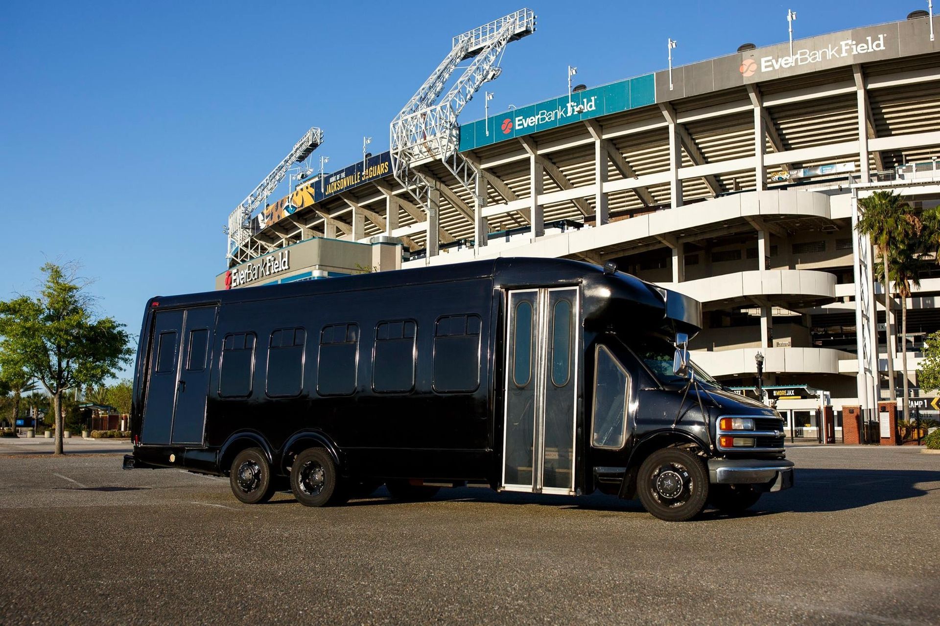 Black tour bus parked outside a stadium under a clear blue sky
