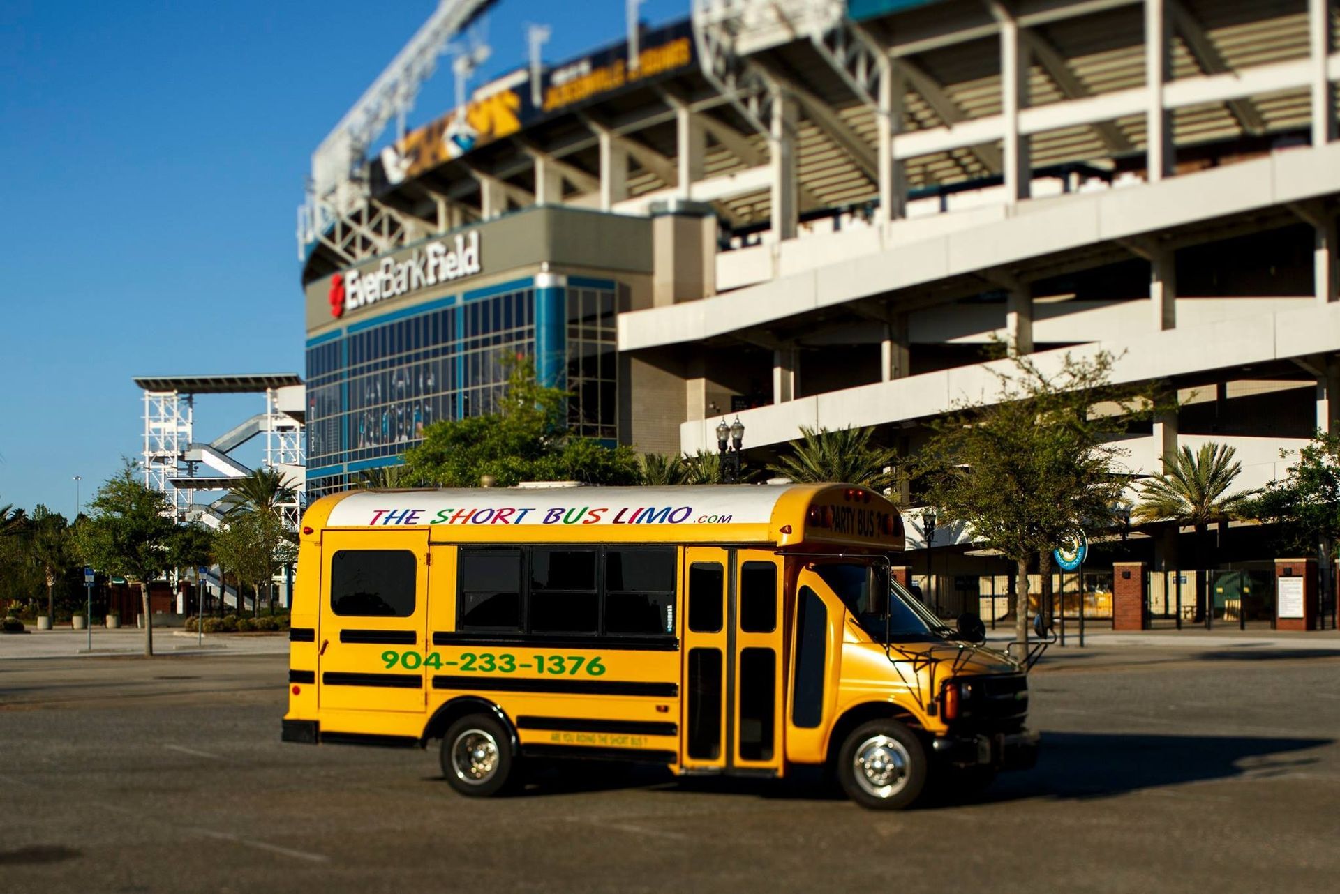 Yellow school bus parked outside a stadium entrance on a sunny day