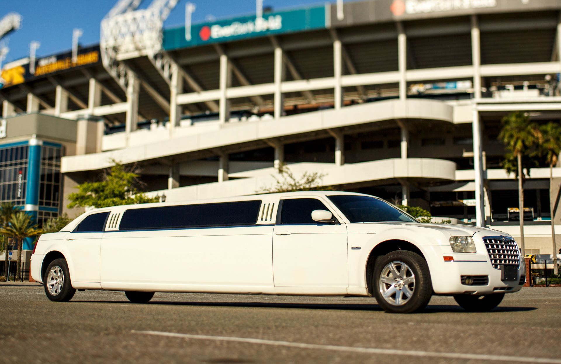 White stretch limousine parked outside a stadium entrance on a sunny day