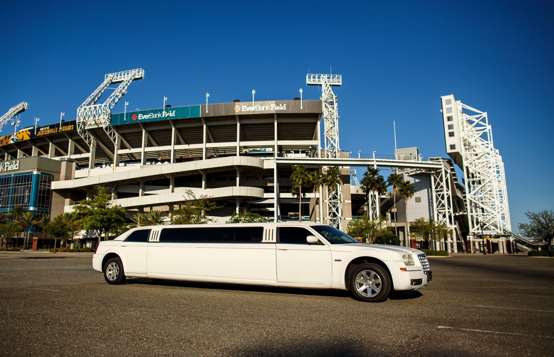 White stretch limousine parked in front of a stadium under a clear blue sky