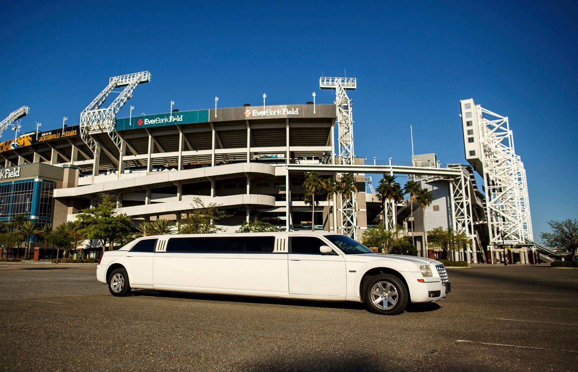 White limousine parked in front of a stadium under a clear blue sky