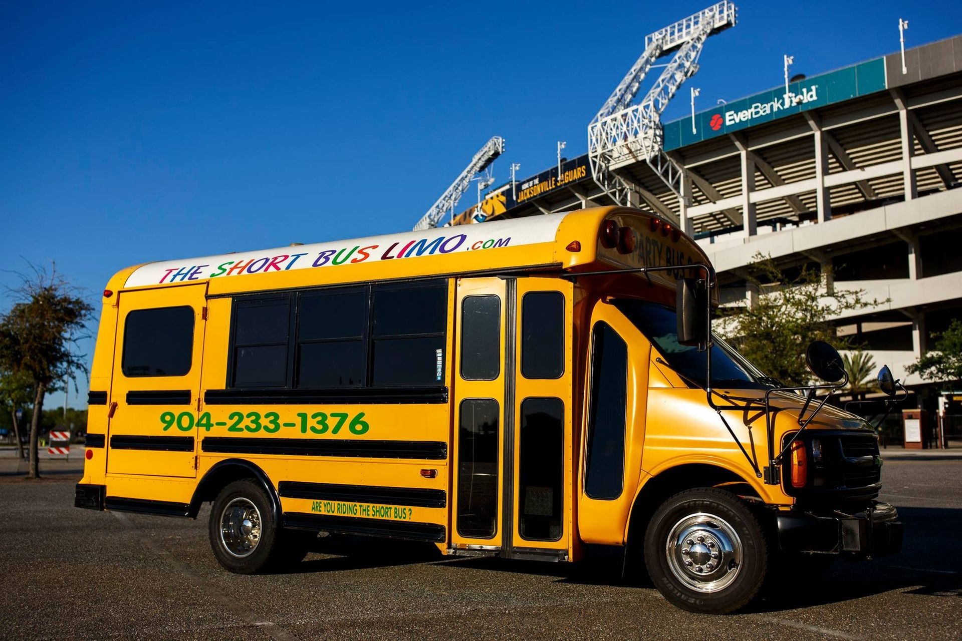 Yellow school bus parked outside a stadium under a blue sky