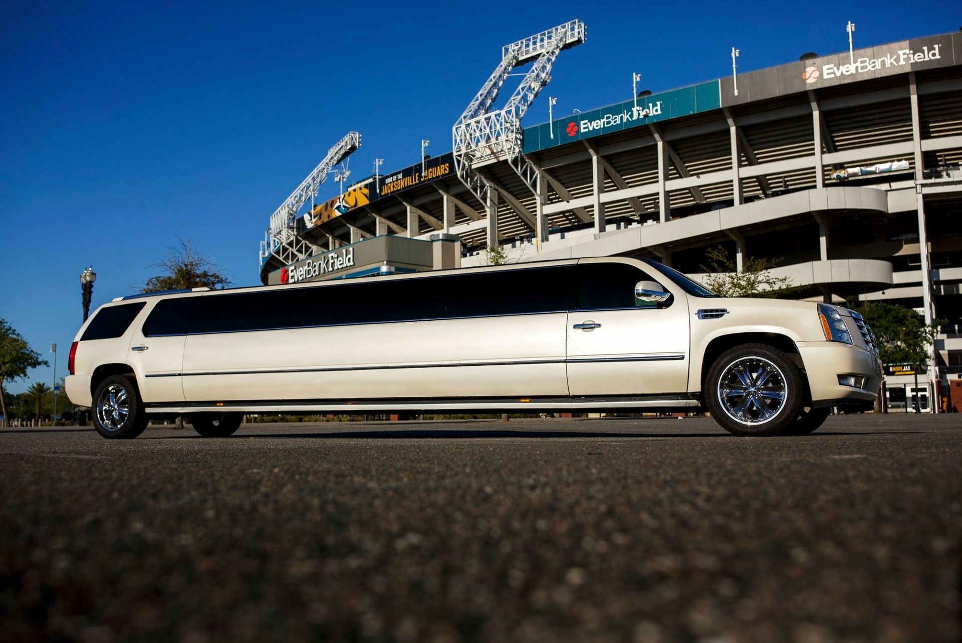 White stretch limousine parked outside a stadium under a blue sky
