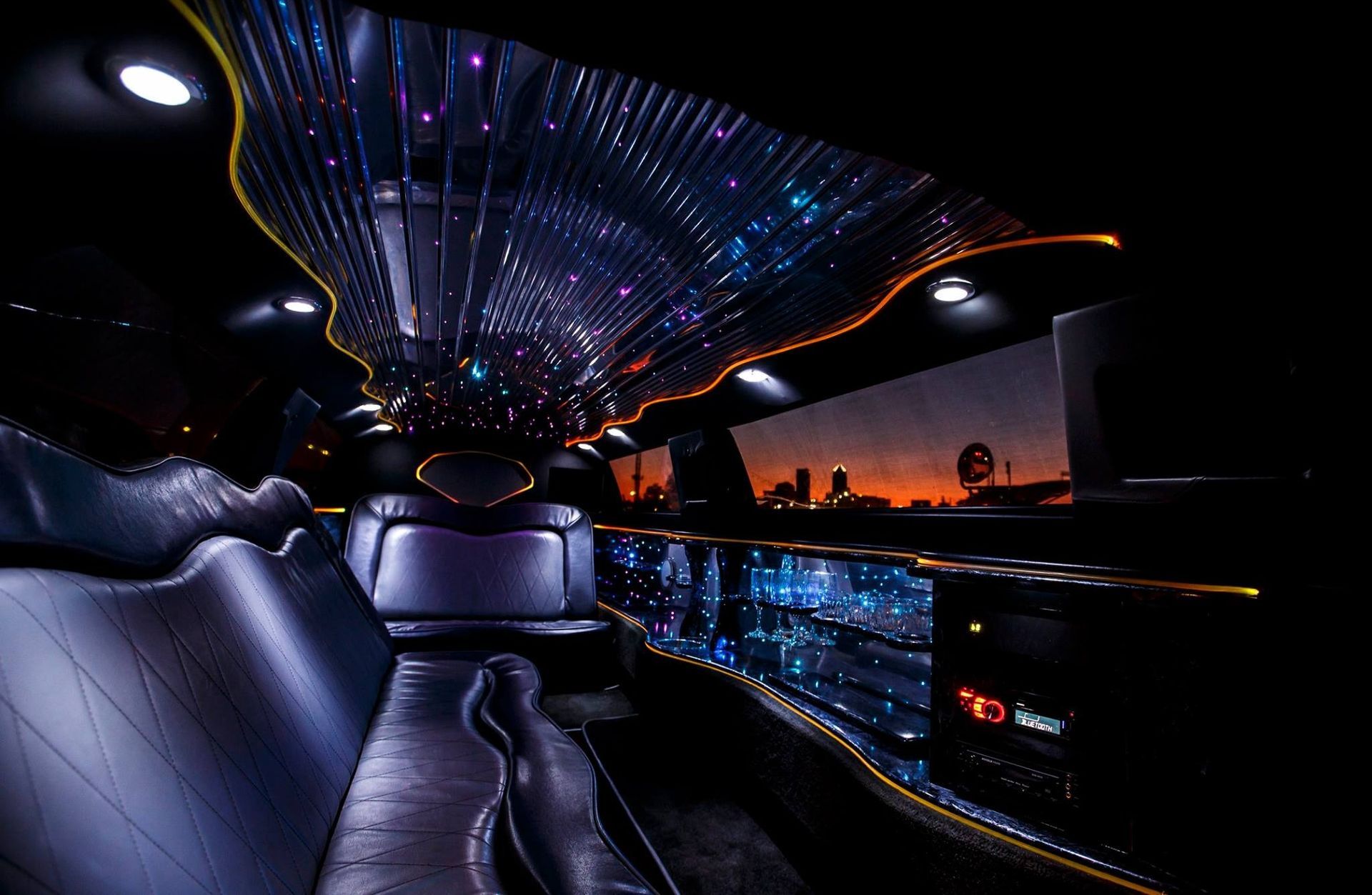 Luxurious limousine interior with blue-purple starry ceiling lights and city lights outside at dusk
