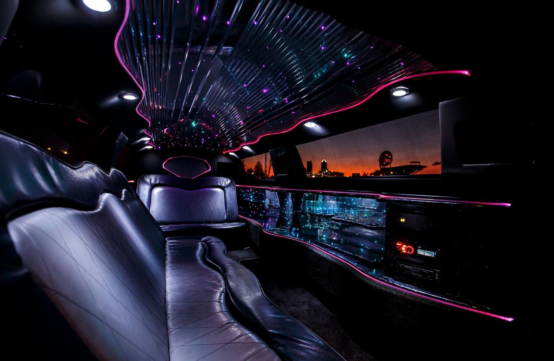 Futuristic limousine interior with neon purple-blue lighting and a city sunset view through the windows
