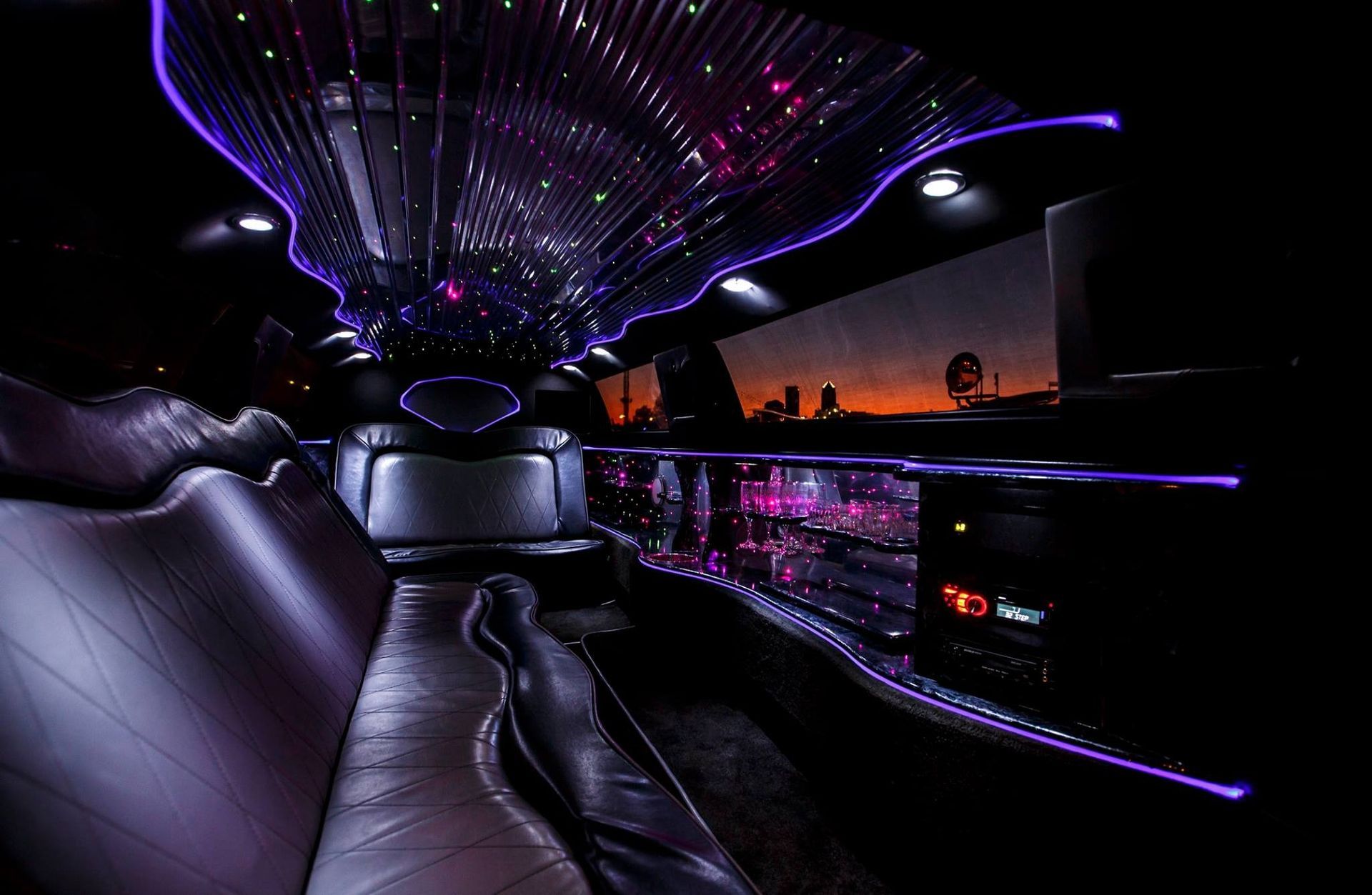 Luxury limousine interior with purple LED lights and sunset city view through the windows
