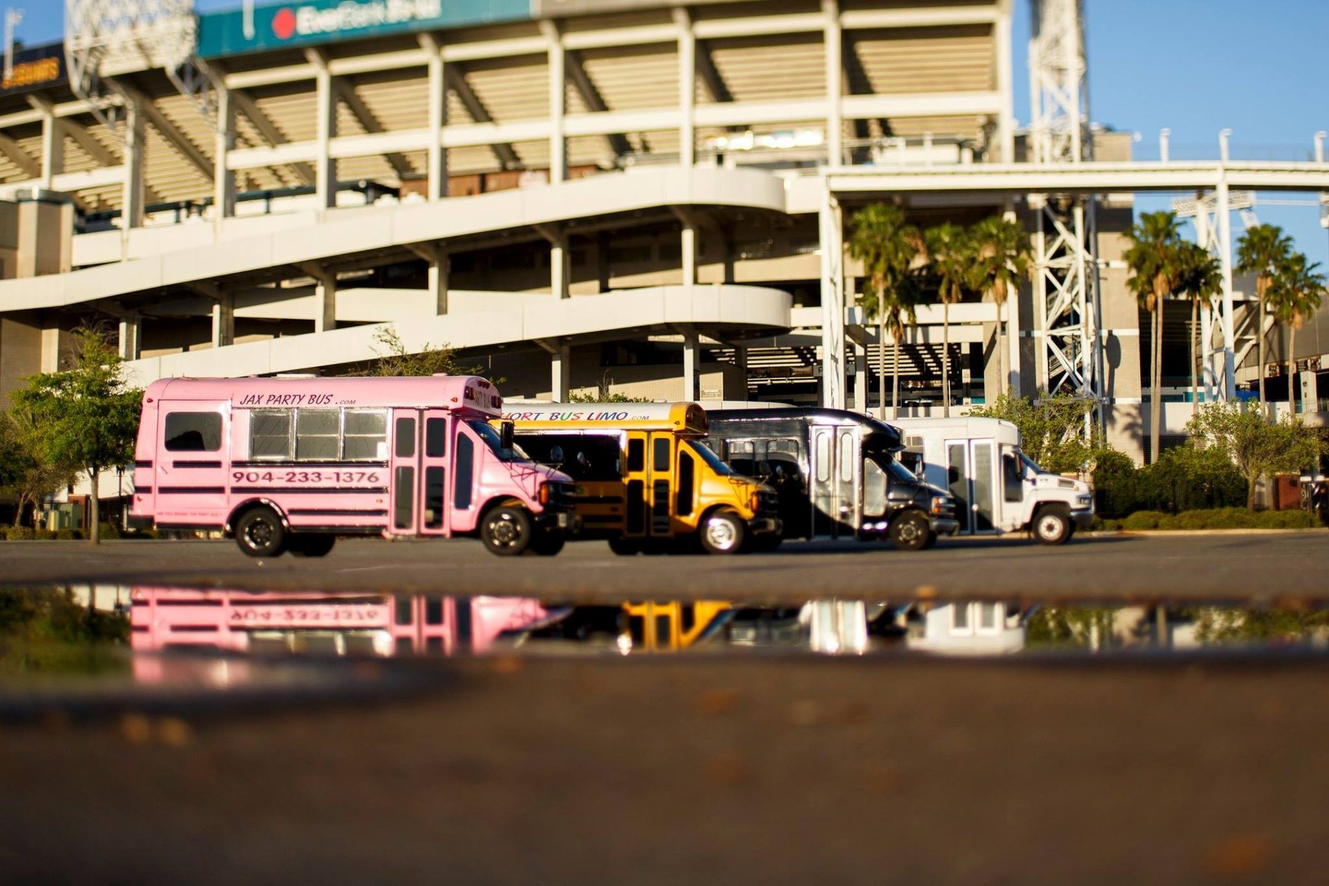 Three colorful buses parked outside an airport terminal, reflected in a wet foreground.
