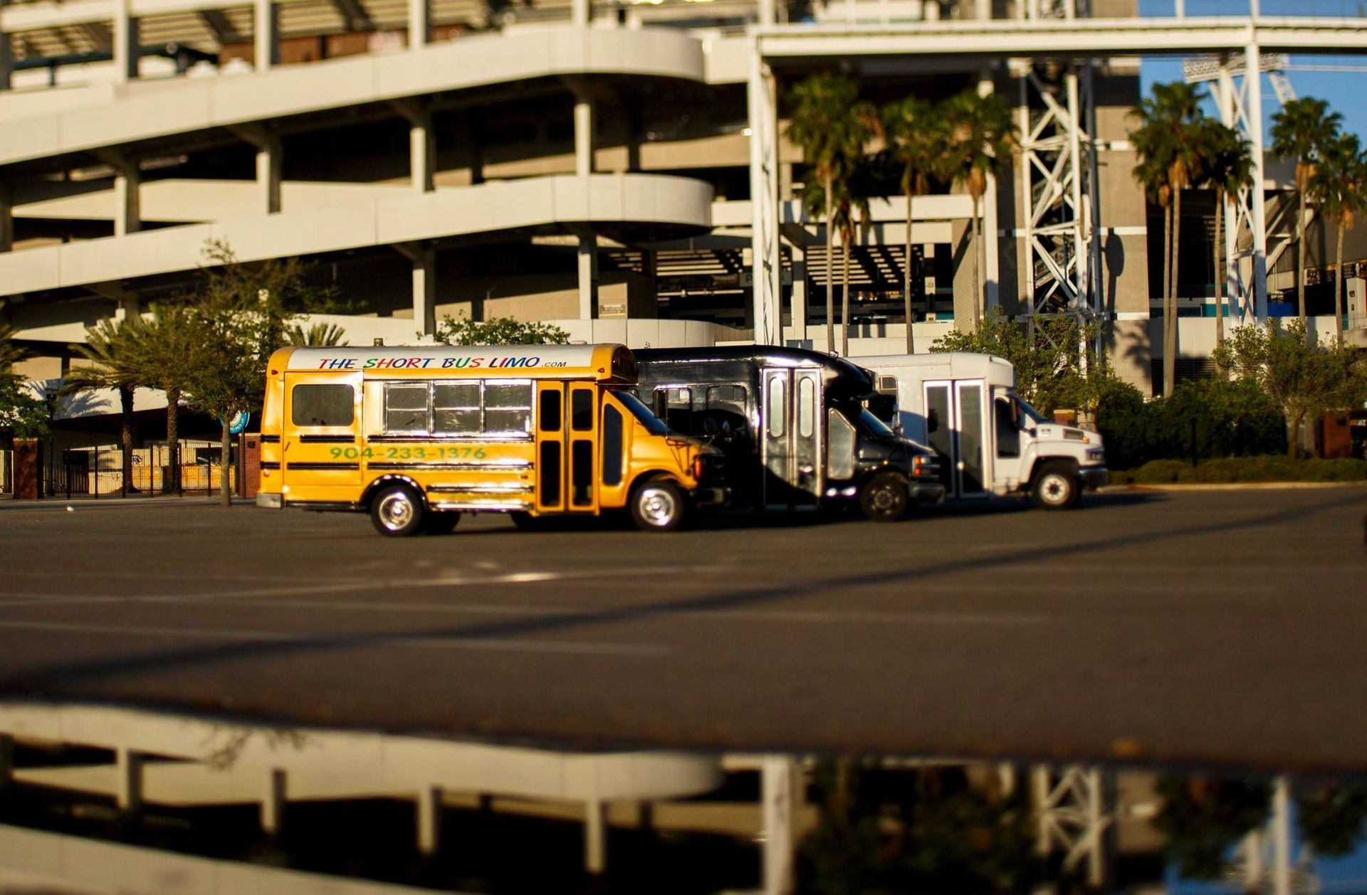 Yellow shuttle buses parked outside a multi-level parking structure, with palm trees in the background.