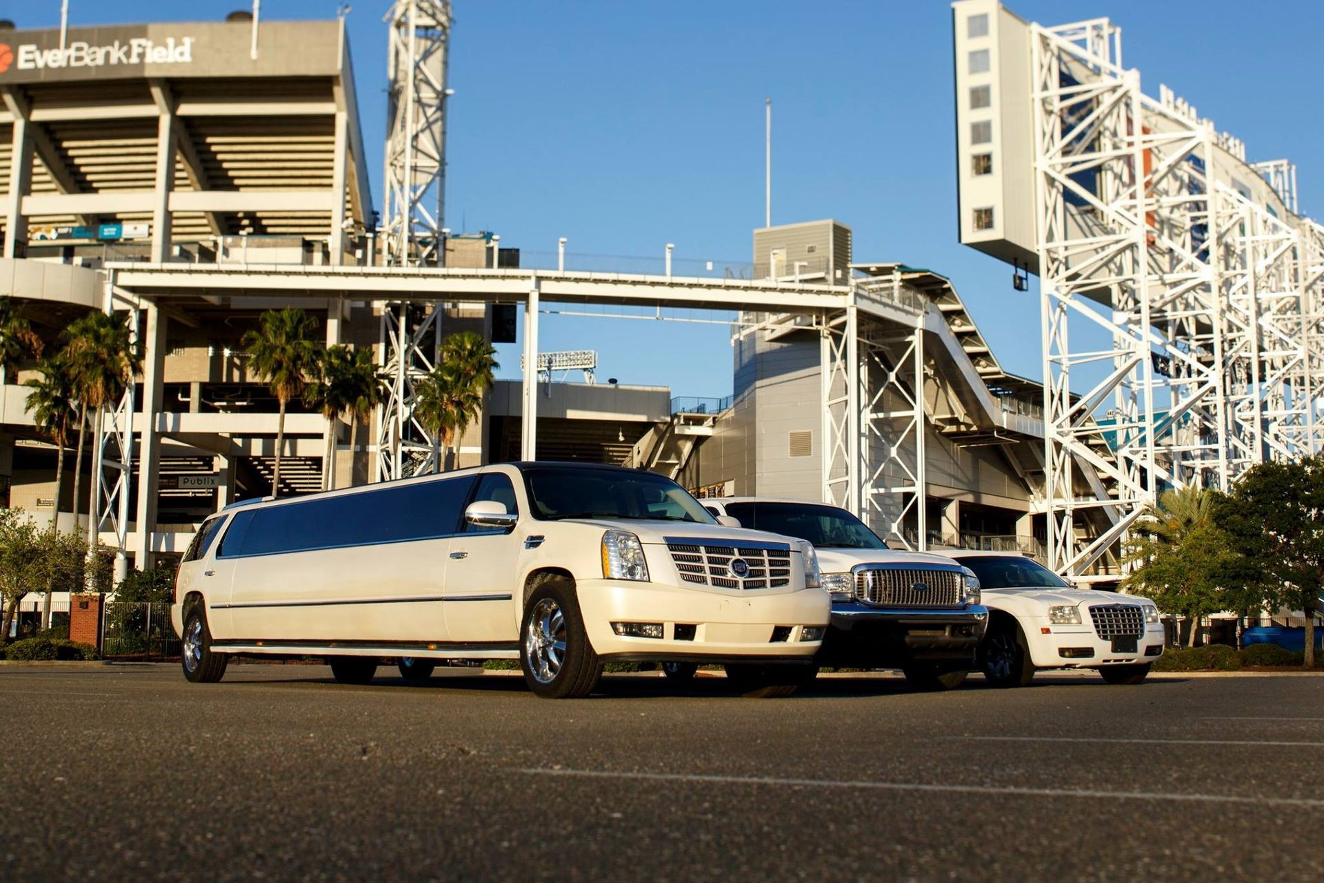 Two white luxury cars parked outside a stadium with elevated walkways in the background