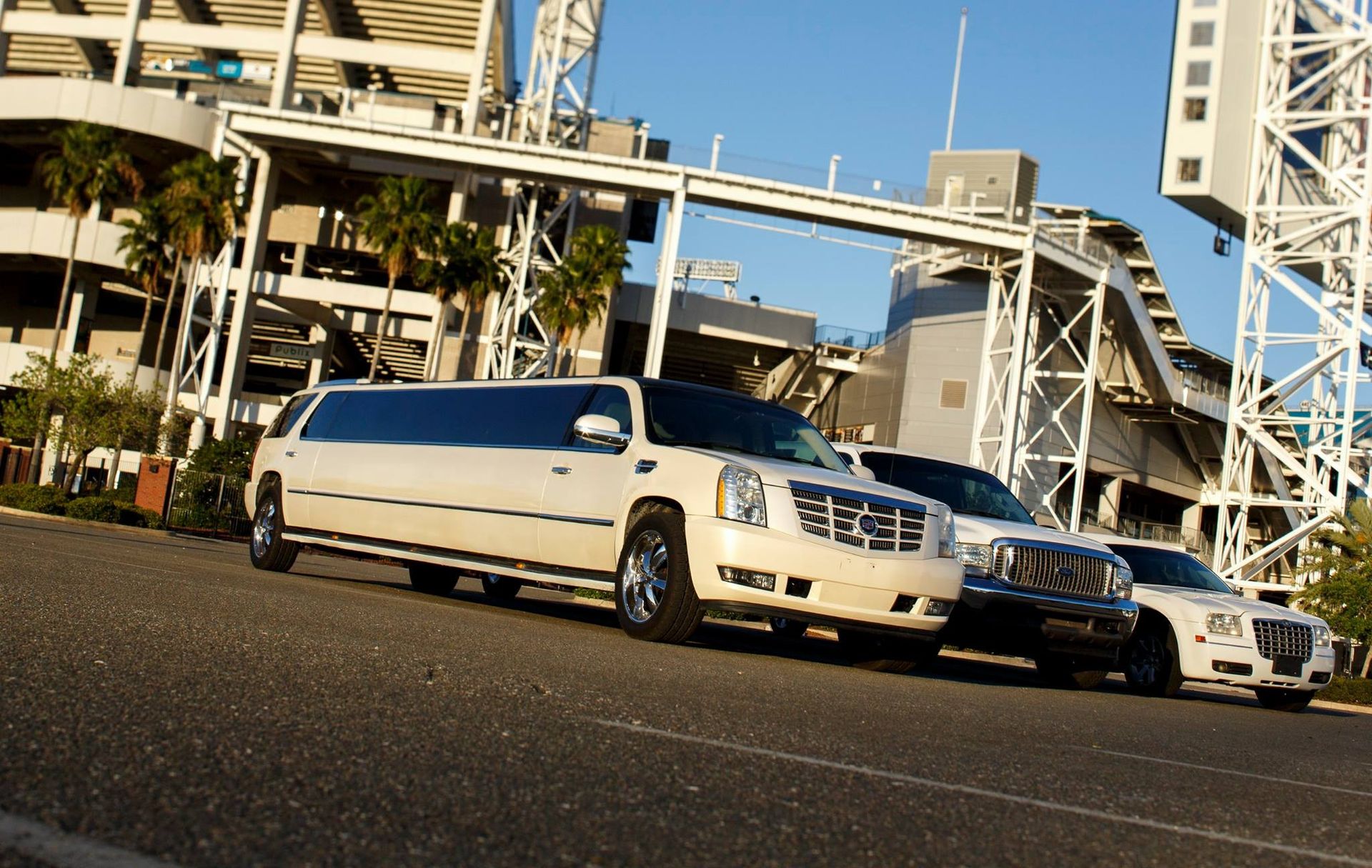 Three luxury cars parked in front of a modern stadium structure