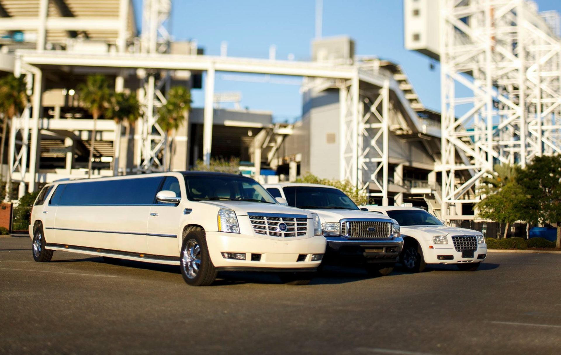 White stretch limousine and two cars parked outside an industrial building under a clear sky