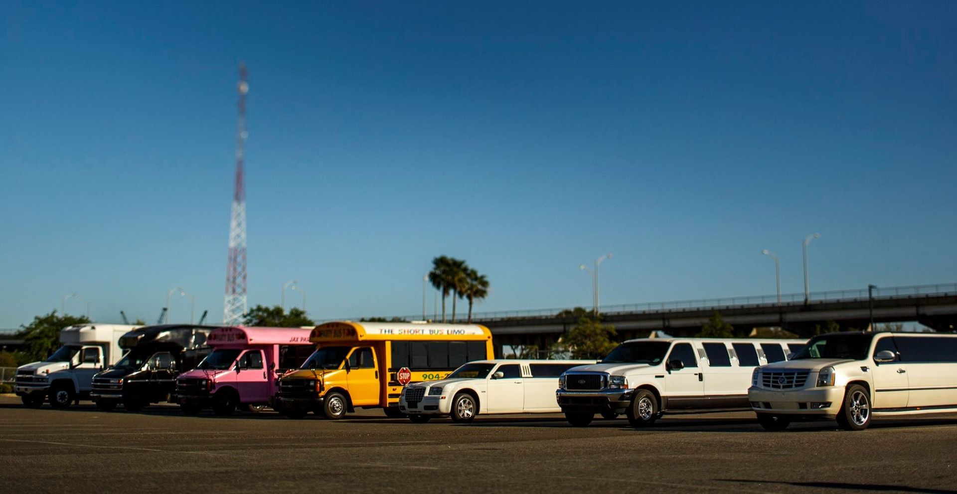 Parked vans and cars along a road under a clear blue sky, including a bright pink and yellow bus.