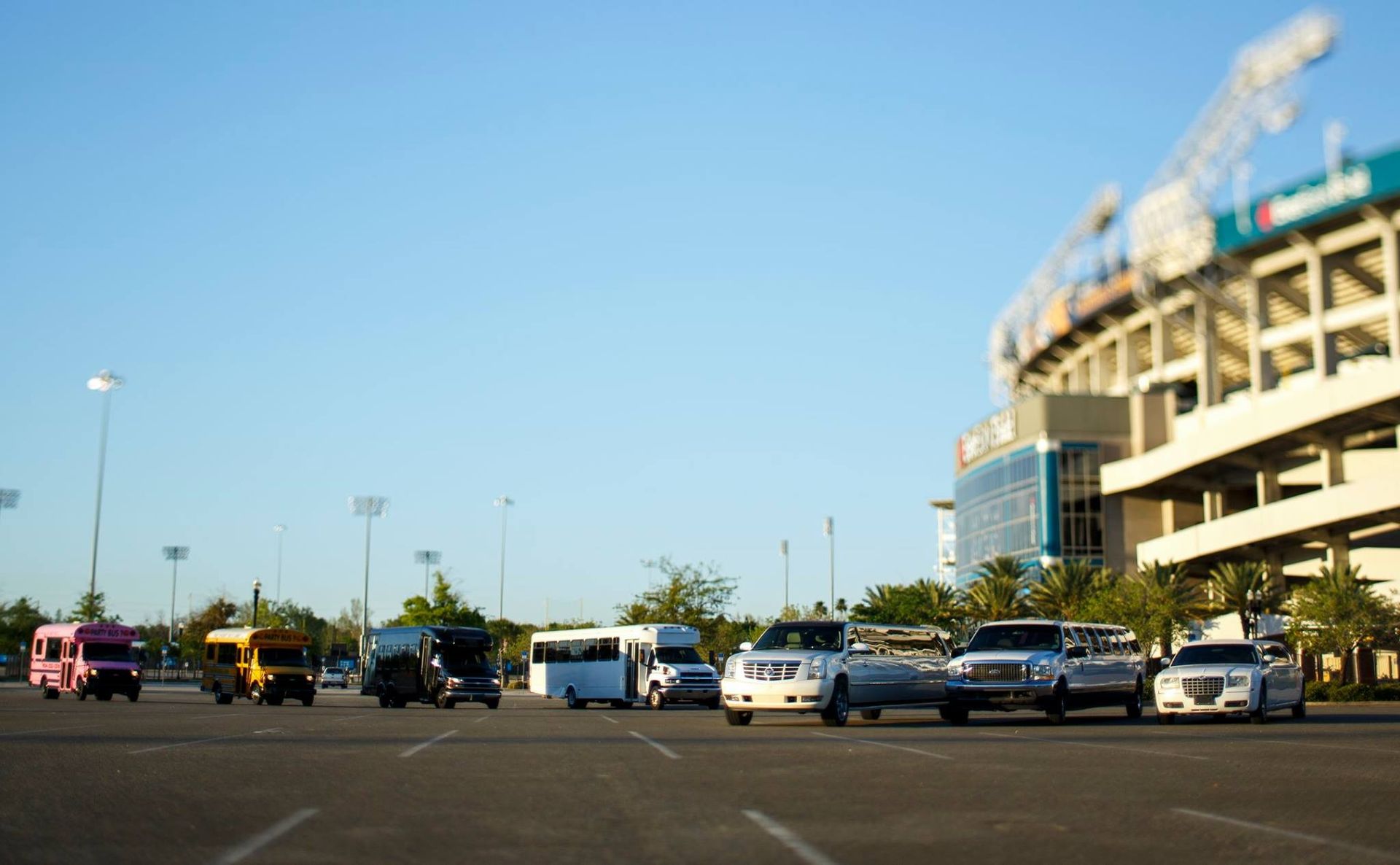 Cars parked in a lot beside a large stadium under a clear blue sky