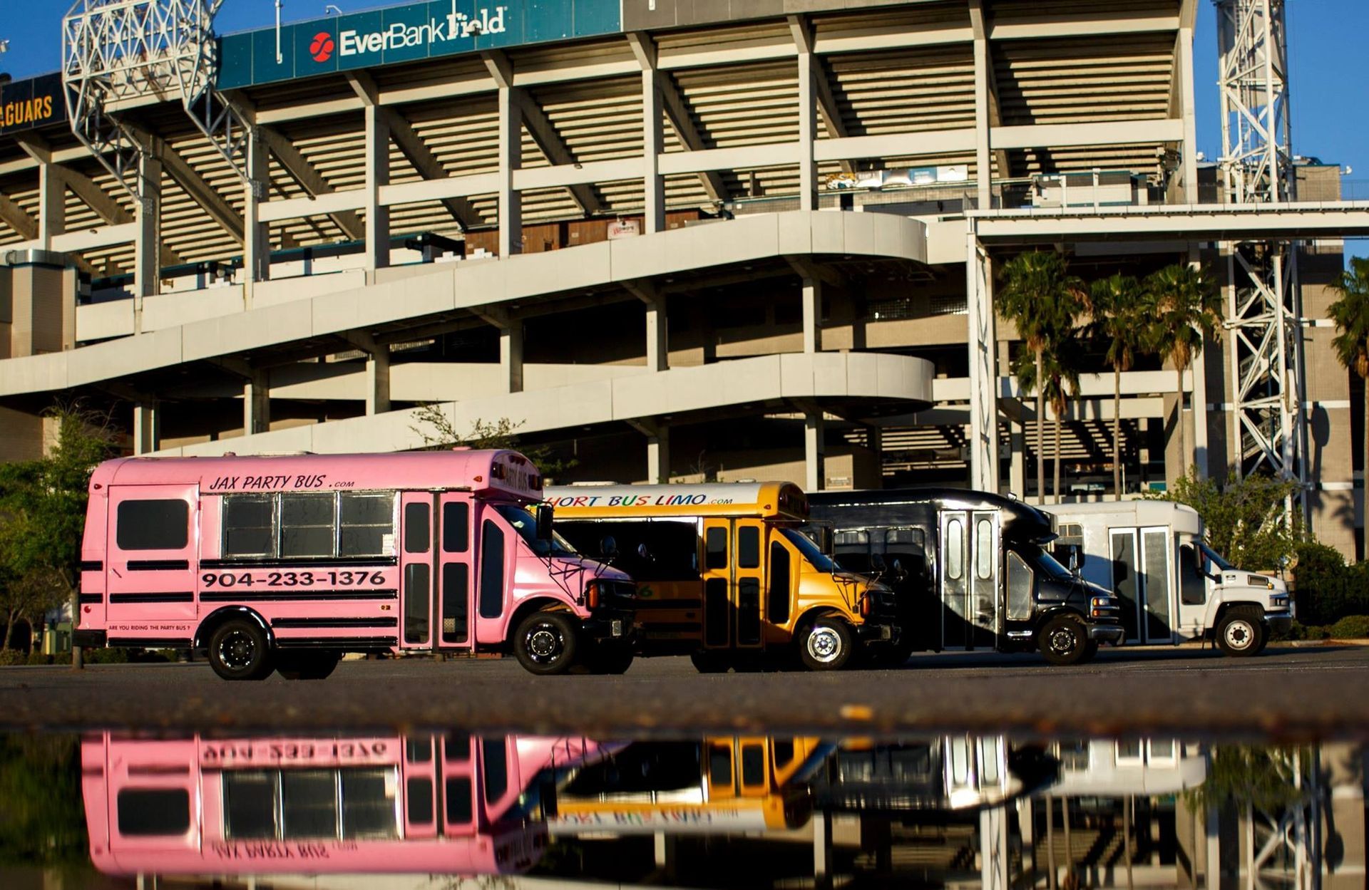 Colorful utility trucks parked in front of a stadium, reflected in a puddle