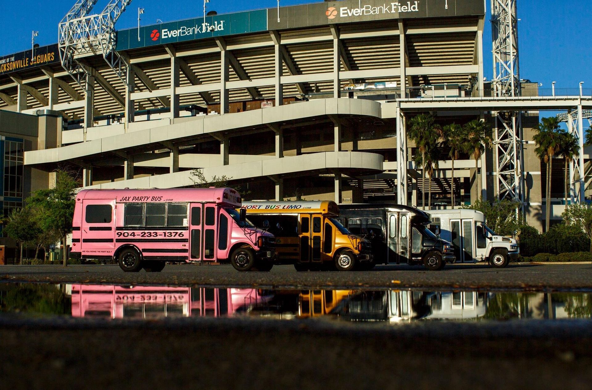 Pink and yellow service trucks parked outside a stadium entrance, reflected in a wet road