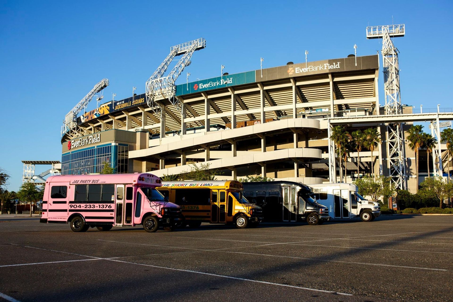 Pink bus and several vehicles parked outside a large stadium under construction.