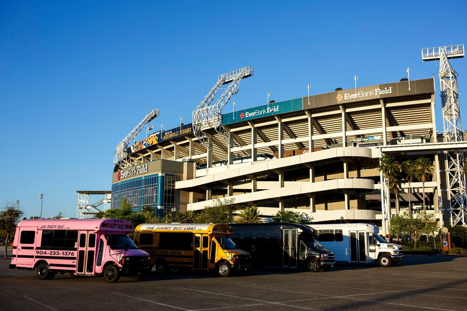 Parked buses and trucks in front of a large stadium under a clear blue sky