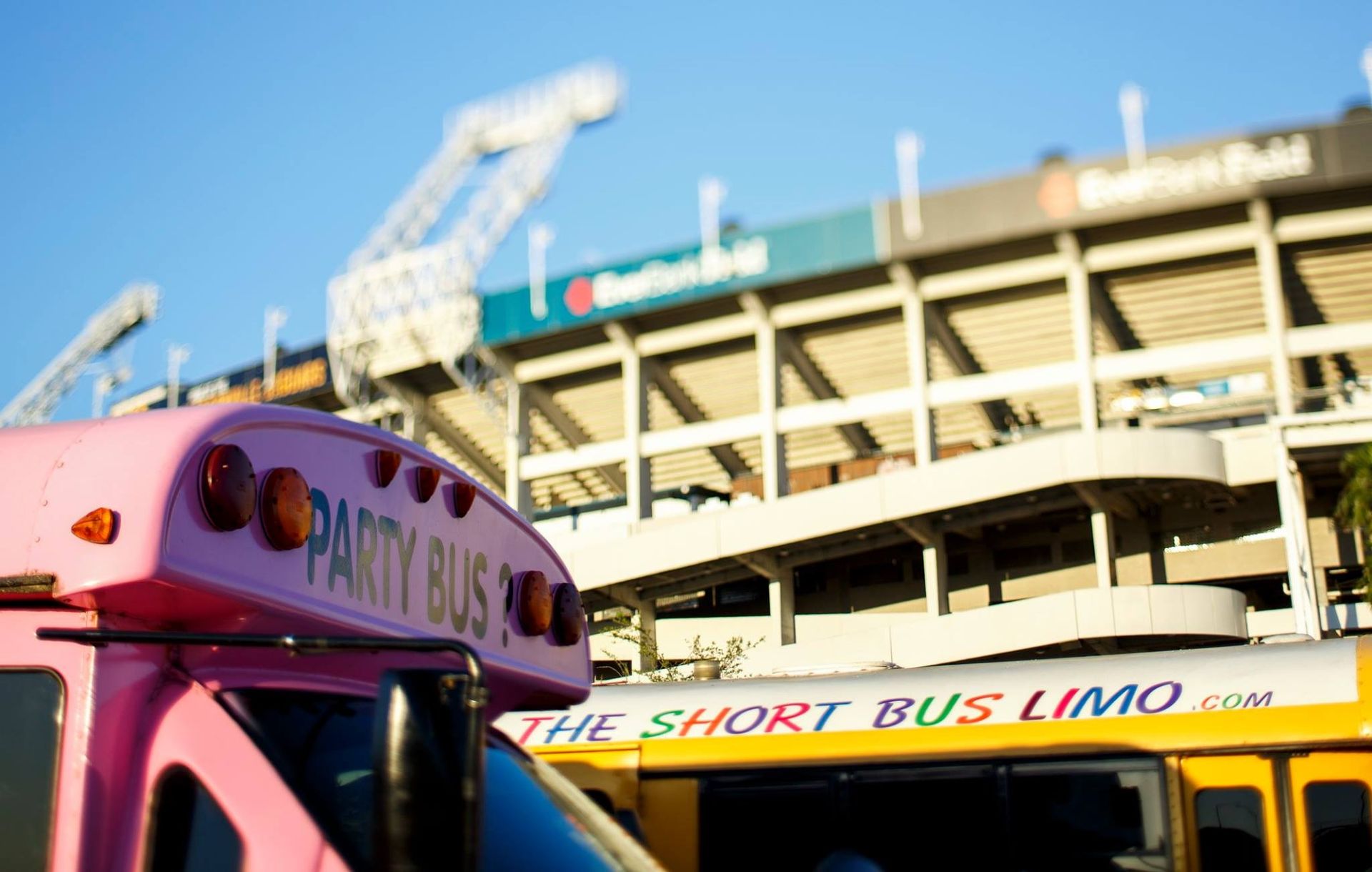 Pink and yellow buses parked outside a transit stadium under a blue sky
