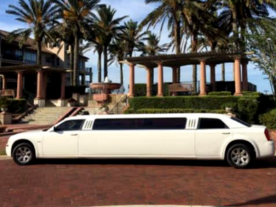 White stretch limousine parked in front of palm trees and a red-brick building on a sunny day