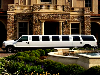 White stretch limousine parked in front of a stone mansion with a fountain and landscaped garden