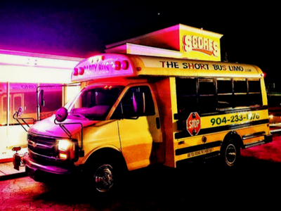 Yellow “The Short Stop” tow truck parked outside a neon-lit storefront at night