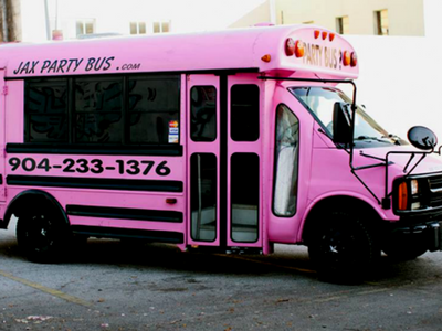 Pink party bus parked on a street with black text and phone number on the side