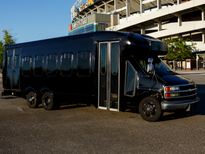 Black shuttle bus parked outside a building, with a blue sky overhead.