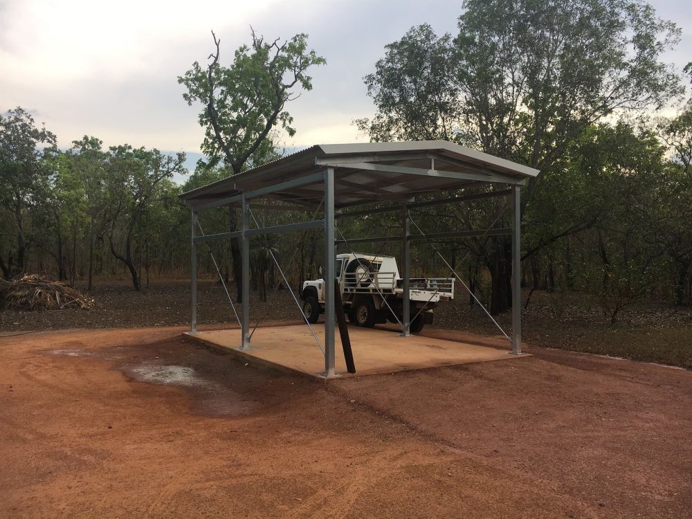 A truck is parked under a metal structure in the middle of a dirt road.