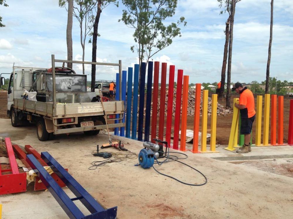 A Man is Working on a Colorful Fence in Front of a Truck — AKS Welding & Fabrication in Winnellie, NT