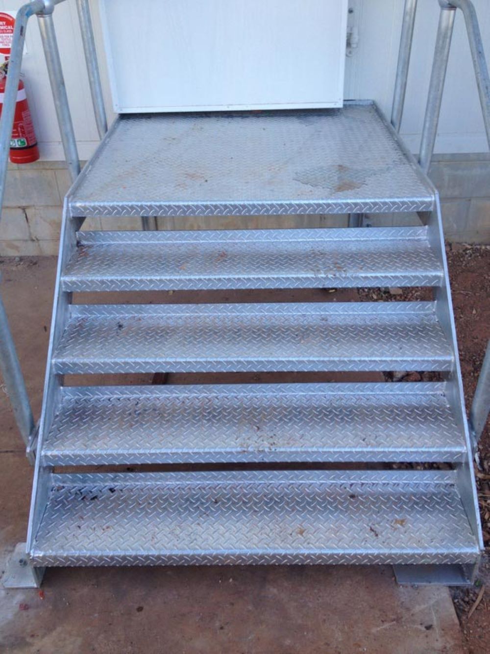 A Set of Metal Stairs Leading Up to a White Door — AKS Welding & Fabrication in Winnellie, NT